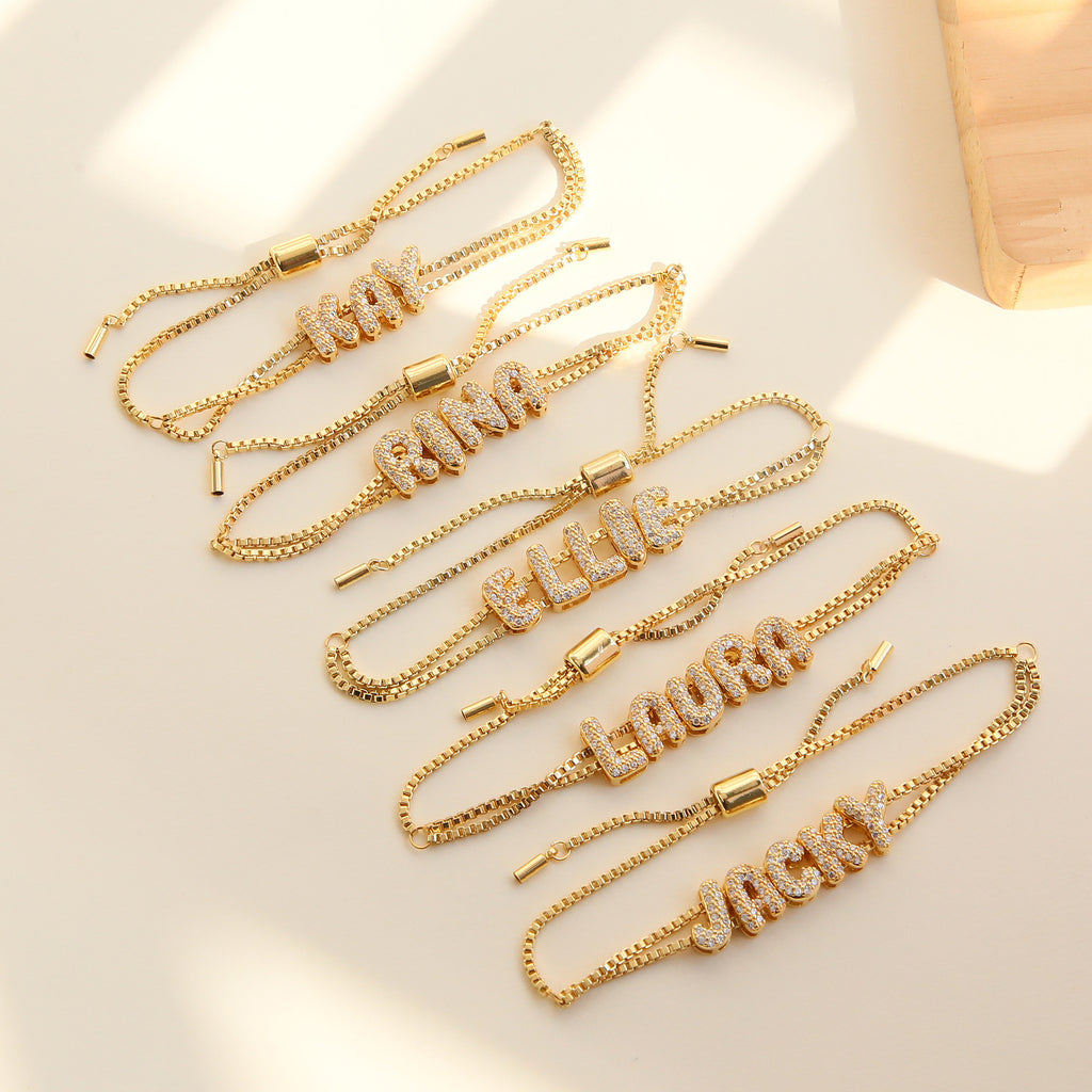 Gold chain bracelets with engraved names on a light background