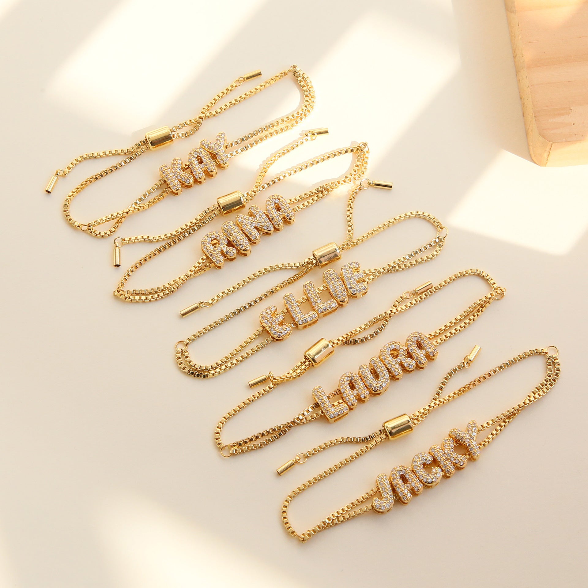 Gold chain bracelets with engraved names on a light background